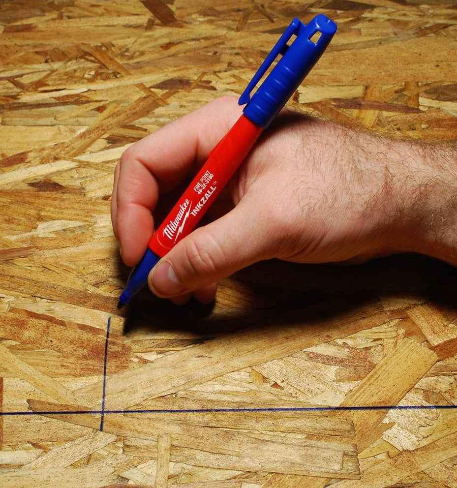 Hand marking rough OSB surface with blue fine point jobsite marker from woodworking tools collection