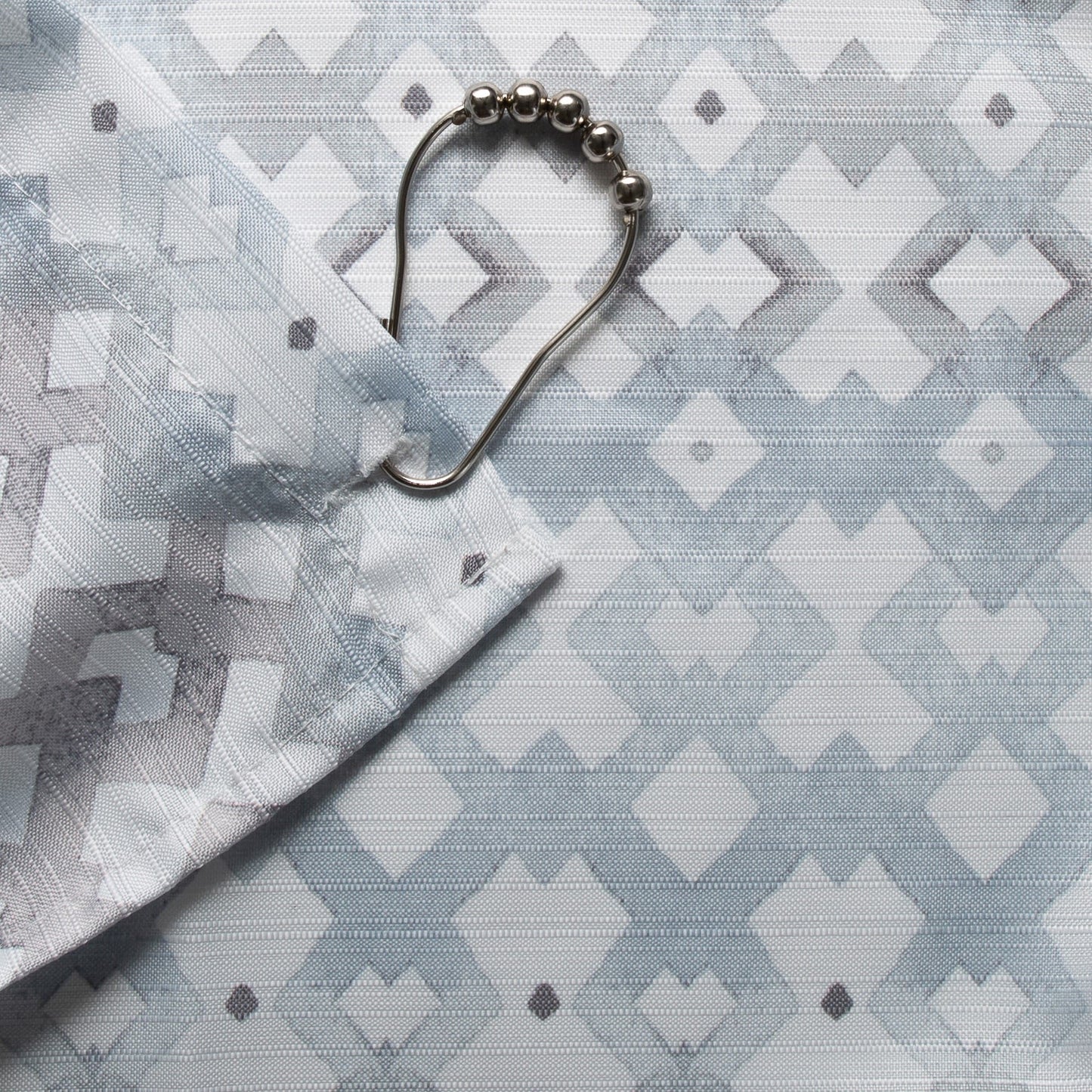 Close-up of grey and blue textured fabric with geometric pattern and metal shower curtain ring for home improvement