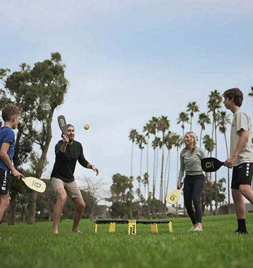 Group of four adults playing with Spikeball SpikePaddle Kit on green grass in outdoor games setting