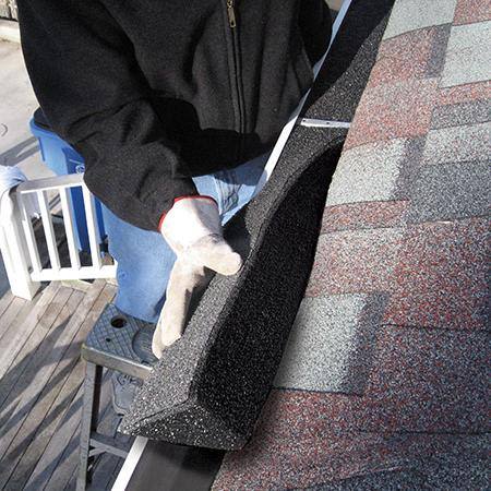 Person wearing gloves installing black foam gutter guard strip on a roof edge for home improvement project