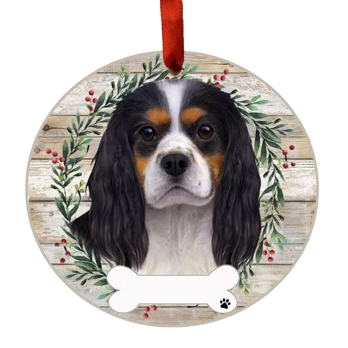 Round Christmas ornament featuring a tri-color King Charles Cavalier face with wreath and red hanging ribbon