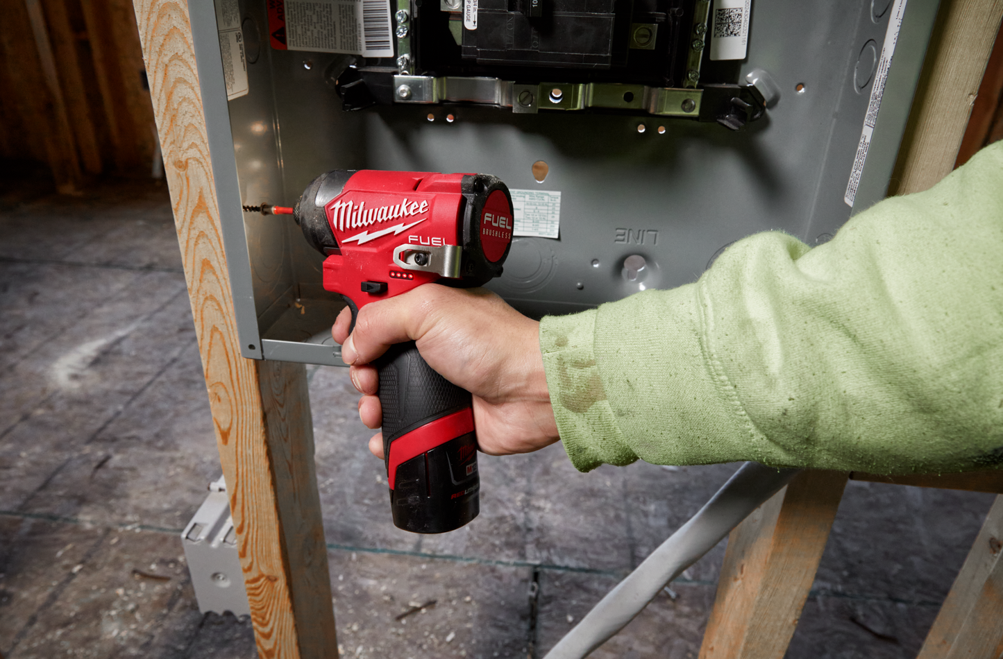 Hand using compact red and black Milwaukee cordless impact driver on electrical panel in home improvement setting