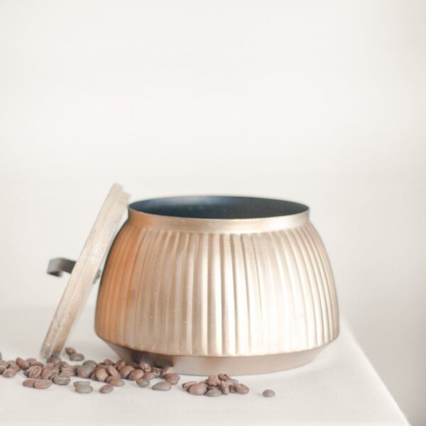 Brass planter with lid and ribbed design set on table with scattered coffee beans in home accents and decor collection