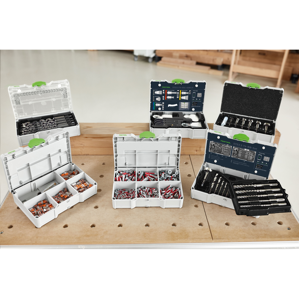 Open modular storage boxes containing various drill bits and woodworking accessories on a workshop table