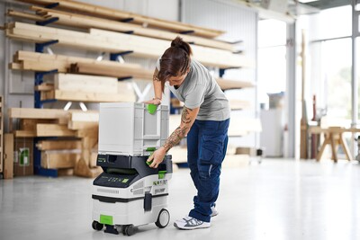 Person organizing a compact white and green Festool modular storage unit in a bright woodworking workshop setting