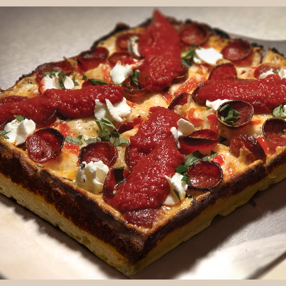 Detroit-style deep dish pizza with pepperoni, ricotta dollops, fresh basil, and tomato sauce on a crispy crust