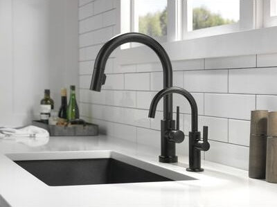 Matte black modern kitchen faucet next to a matching beverage faucet installed on white countertop under window