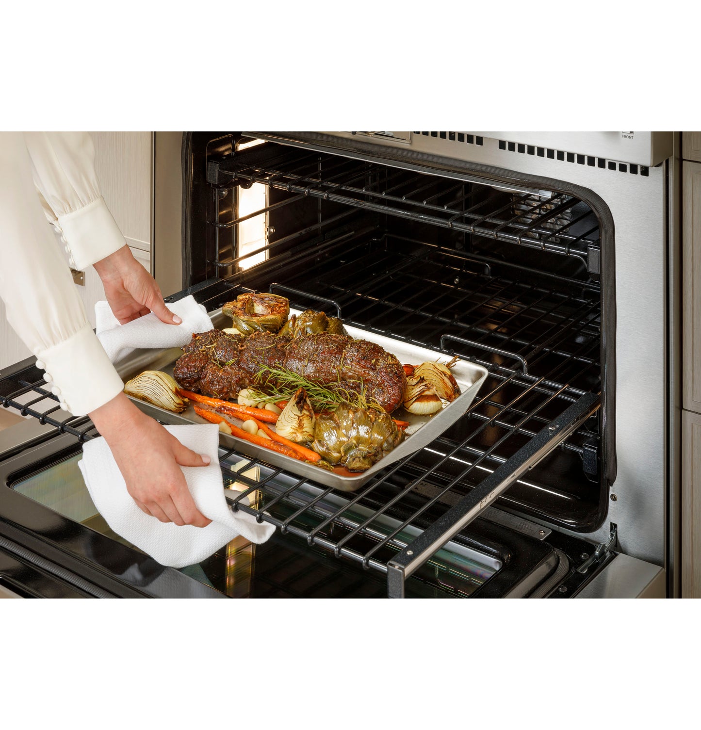 Person removing tray of roasted meat and vegetables from stainless steel oven in kitchen appliances collection