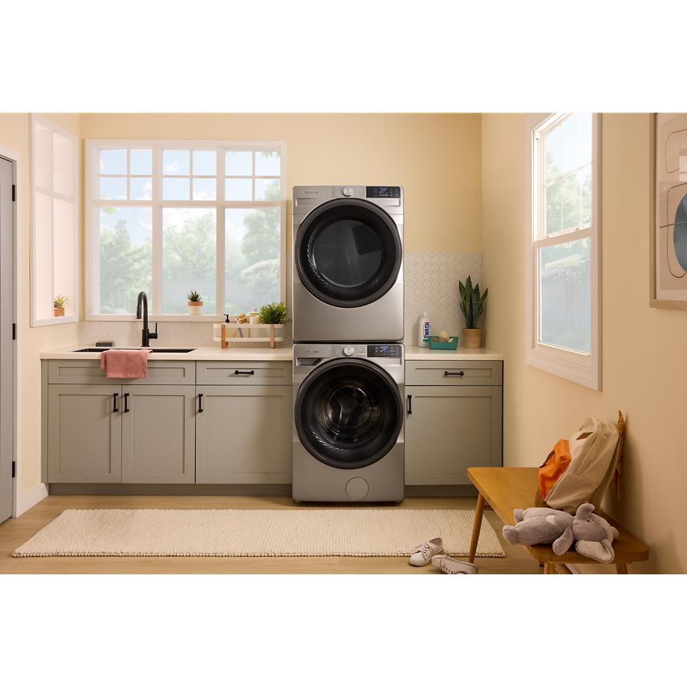 Stacked silver smart front load washer and dryer in beige laundry room with cabinetry and natural light windows