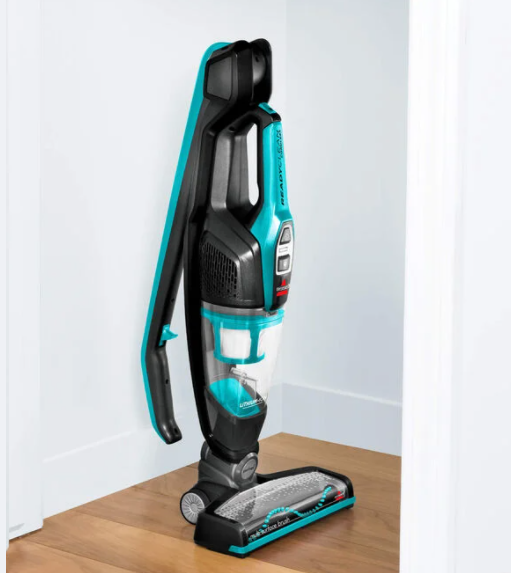 Bissell ReadyClean cordless stick vacuum in electric blue standing on hardwood floor near white wall corner