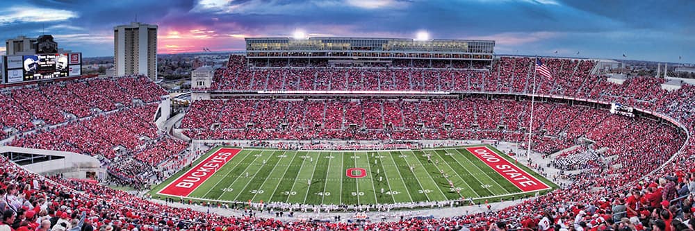 Wide panoramic view of crowded Ohio State University stadium under a colorful evening sky during a football game