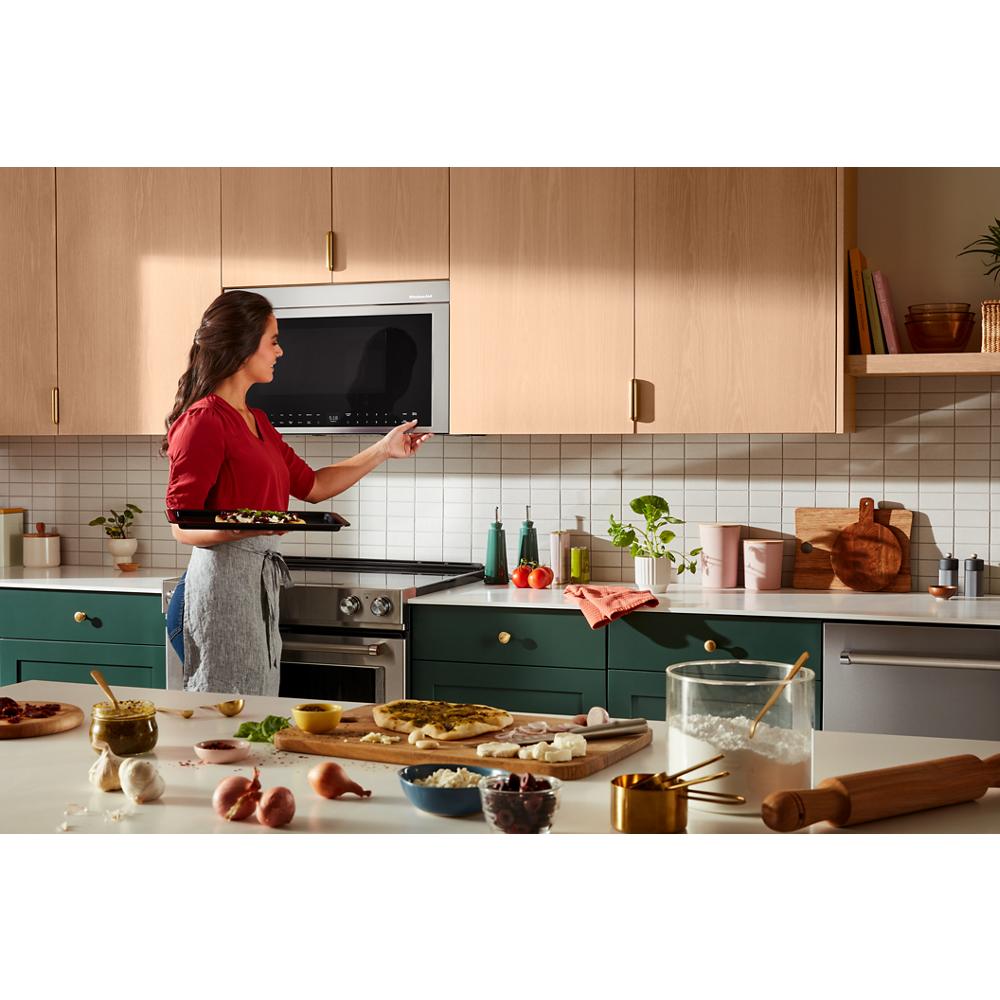 Woman placing a baking tray into a stainless steel KitchenAid multifunction over-the-range oven in a modern kitchen setting