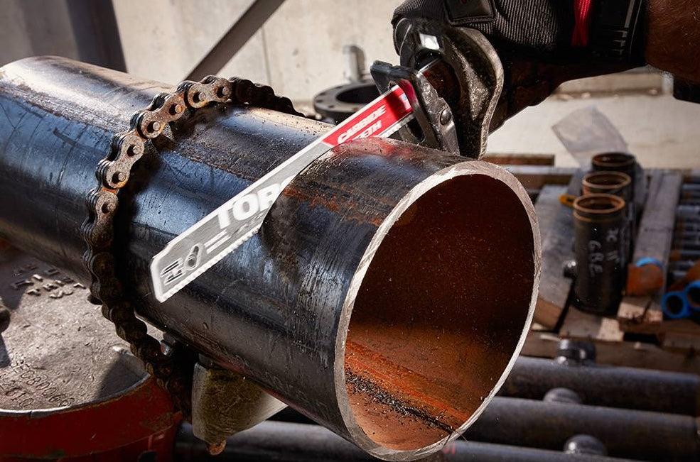 Close-up of a power tool cutting thick metal pipe with a carbide saw blade in a workshop setting.