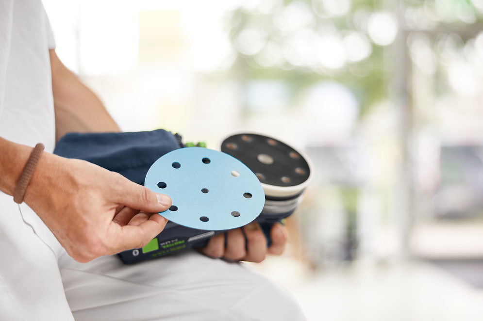 Person holding blue sanding disc ready to attach to cordless random orbit sander for woodworking tools use