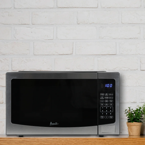 Compact stainless steel microwave with digital control panel and blue LED display on wooden countertop with brick wall background