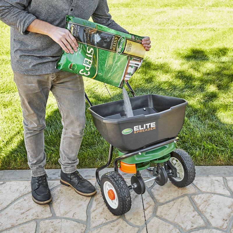Person pouring Scotts lawn food Step 3 into a Scotts Elite spreader for lawn fertilizer application