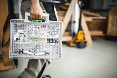 Person carrying transparent modular organizer with adjustable compartments for tool storage in workshop setting