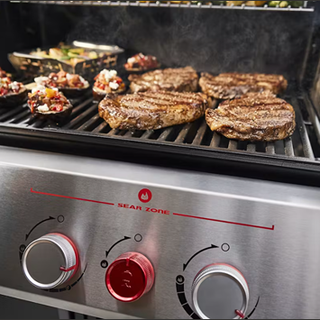 Close-up of grilled steaks and stuffed mushrooms cooking on a black natural gas grill with stainless steel control knobs