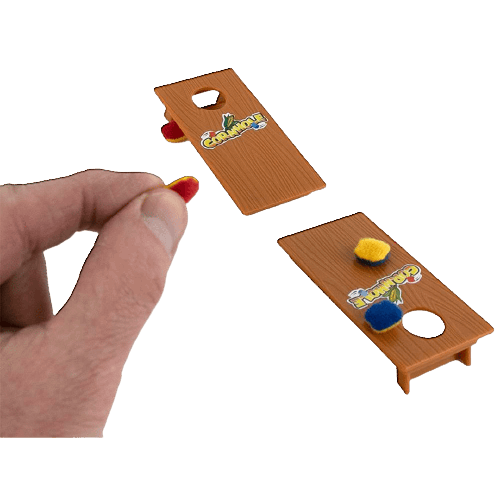 Miniature wooden cornhole boards with colorful bean bags and hand throwing in a casual indoor setting