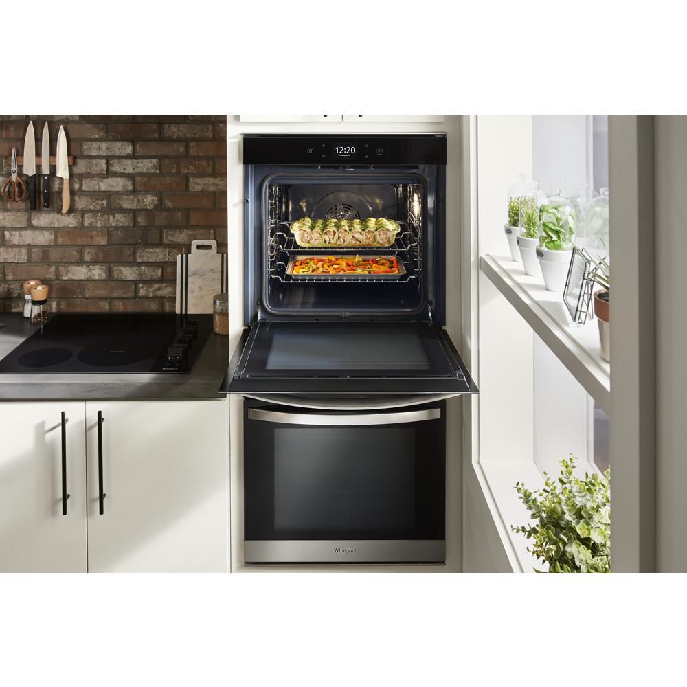 Open wall oven with convection cooking two trays of vegetables in a modern kitchen with white cabinetry and brick backsplash