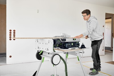 Man operating a cordless table saw mounted on a Festool underframe in a home improvement workshop setting