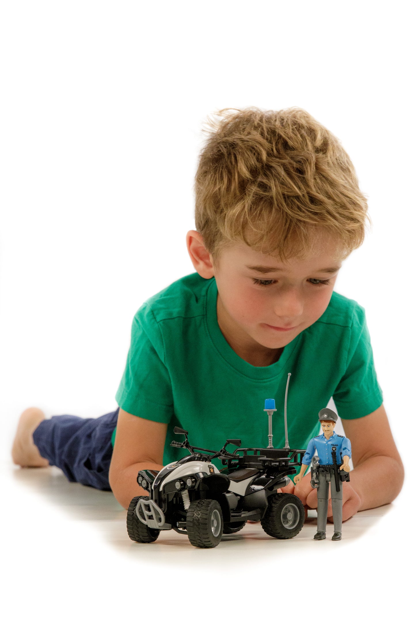 Young boy lying down playing with black police quad toy and light skin officer figure from Bruder Toys collection under $50