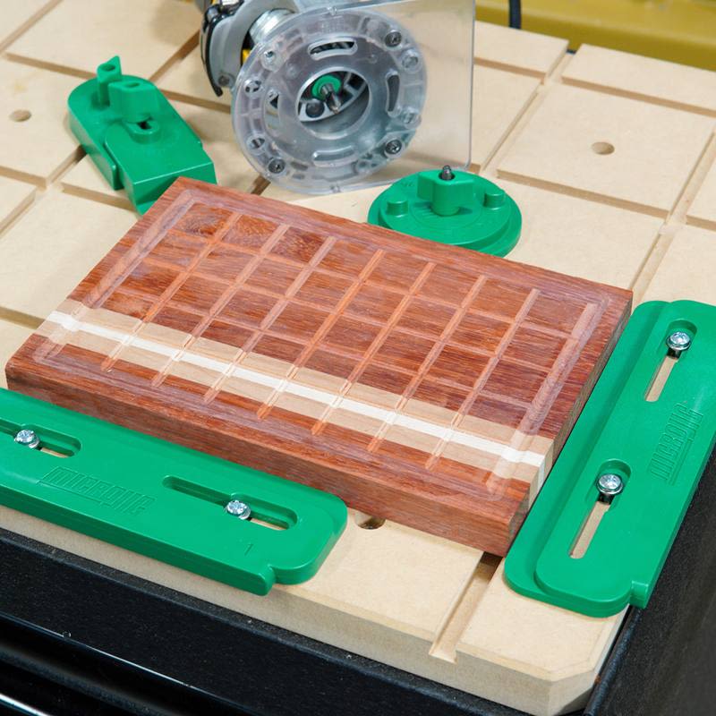 Green plastic CNC workholding components securing a wooden board with routed grid pattern for precision woodworking tasks