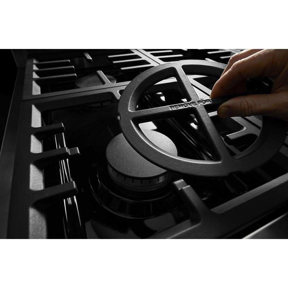 Close-up of black cast iron grate being removed from a burner on a commercial-style dual fuel KitchenAid cooktop