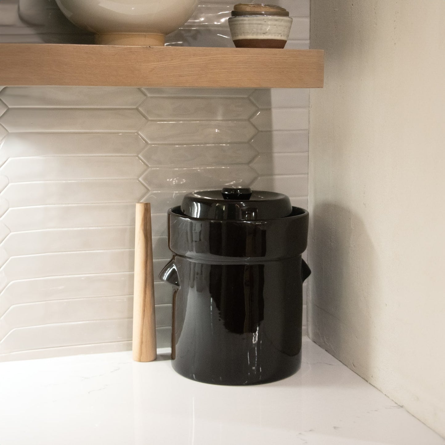 Glossy black ceramic crock with lid and wooden stomper on white countertop in kitchenware and small kitchen appliances collection