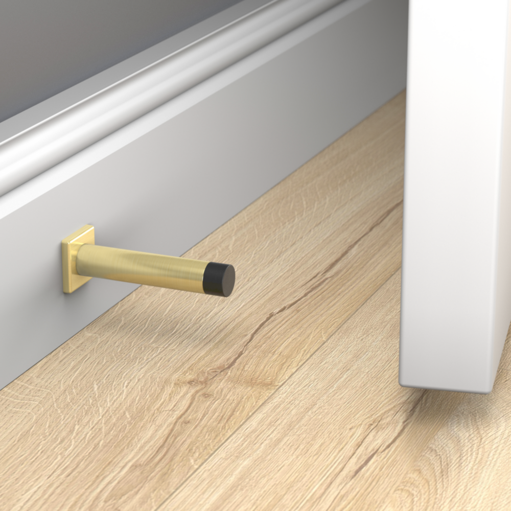 Brushed gold aluminum door stop with black rubber tip mounted on baseboard for wall protection in door accessories collections