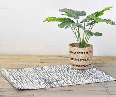 White and grey boho patterned rug laid on wooden floor with woven basket planter holding tropical green leaves