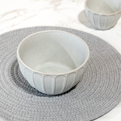 White ceramic bowl with subtle vertical ridges placed on round textured gray placemat in kitchen setting