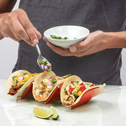 Red and stainless steel taco holder supporting three filled tacos on white countertop in kitchenware collection