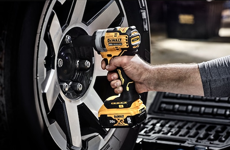 Yellow and black cordless impact wrench tightening lug nuts on vehicle wheel for tools and home improvement
