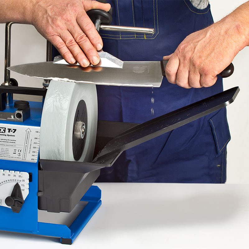 Person sharpening a large kitchen knife on a wet grinding wheel with an advanced water trough for tools