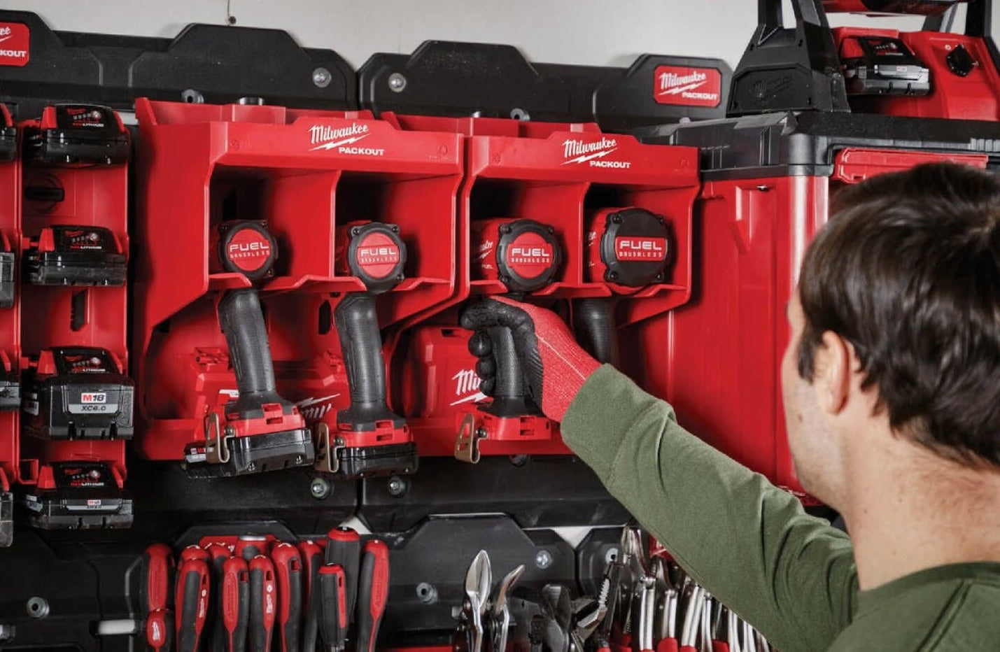 Person organizing red Milwaukee PACKOUT™ tool station with cordless drills and hand tools for home improvement tasks