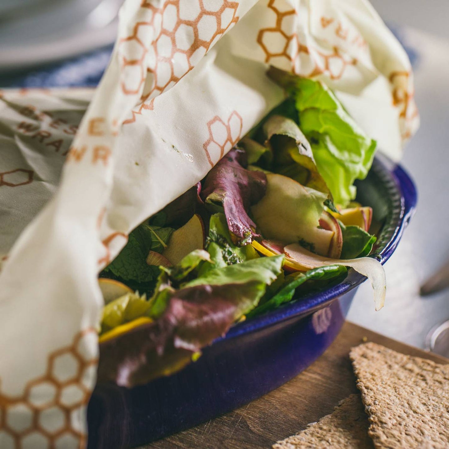 Reusable honeycomb-patterned beeswax wrap covering fresh salad in blue bowl for kitchen storage under $50 collections
