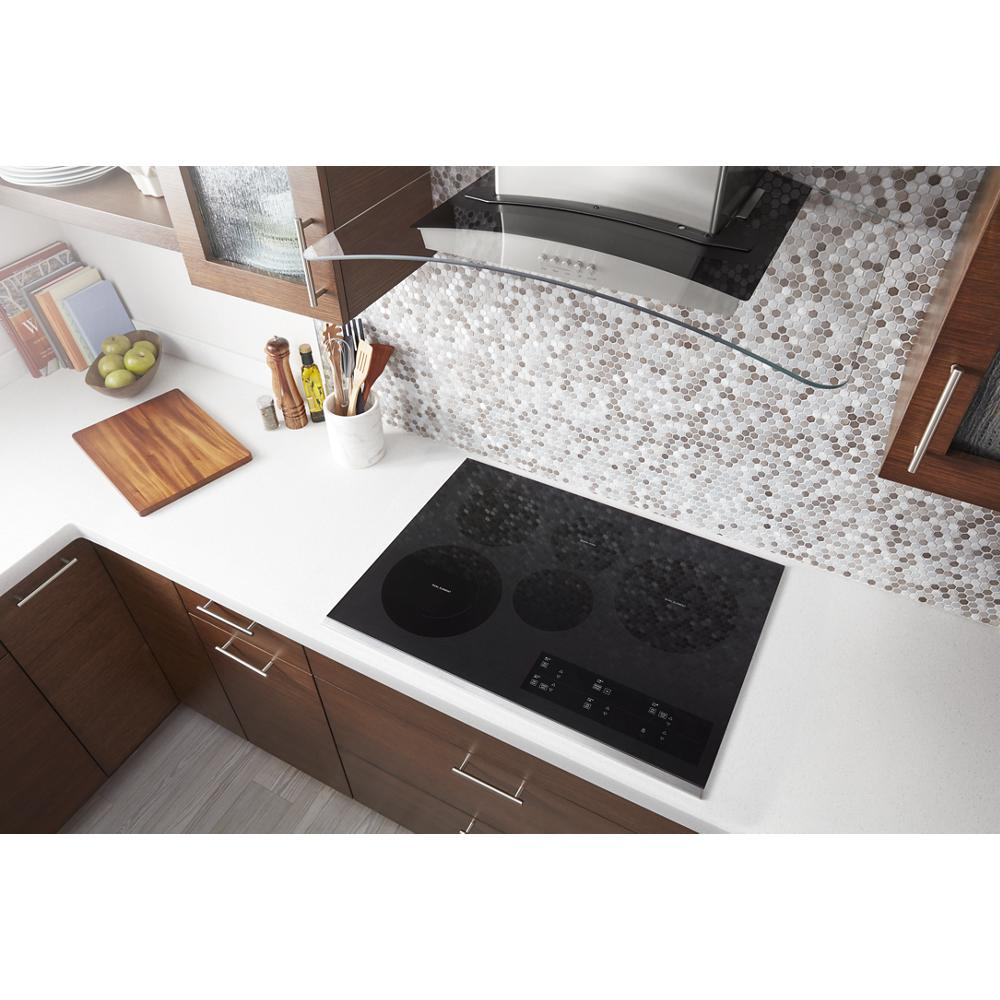 Black electric ceramic cooktop with two dual radiant elements installed on white kitchen countertop in modern kitchen.