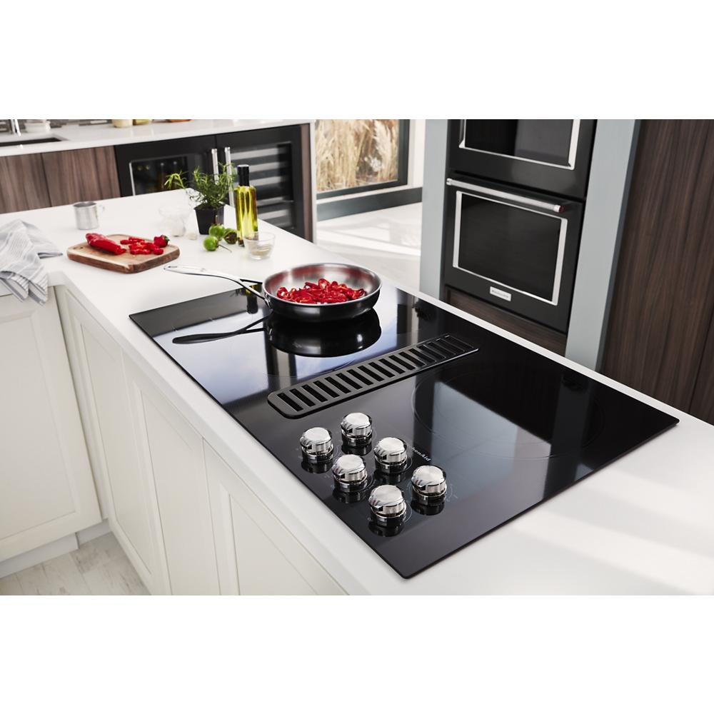 Black electric cooktop with five stainless steel knobs and integrated downdraft vent in modern kitchen setting