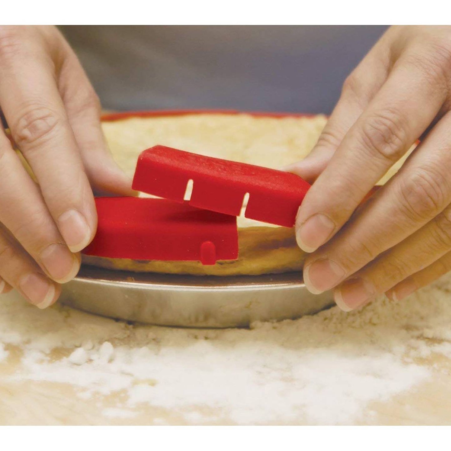 Hands adjusting a red food-safe silicone pie crust shield on an unbaked pie in a kitchenware setting