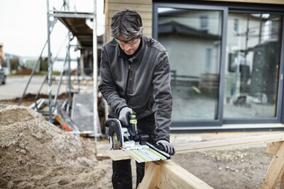 Man using cordless Festool carpentry saw with guide rail cutting wood at outdoor construction site for home improvement