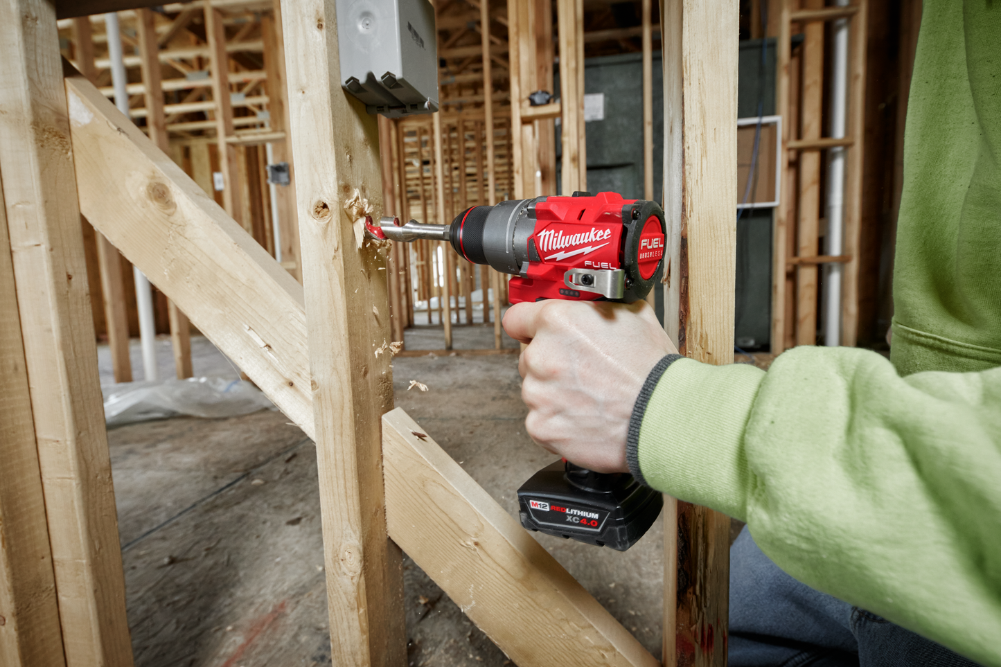 Red and black cordless drill driver being used to install electrical wiring in wooden framing for home improvement.