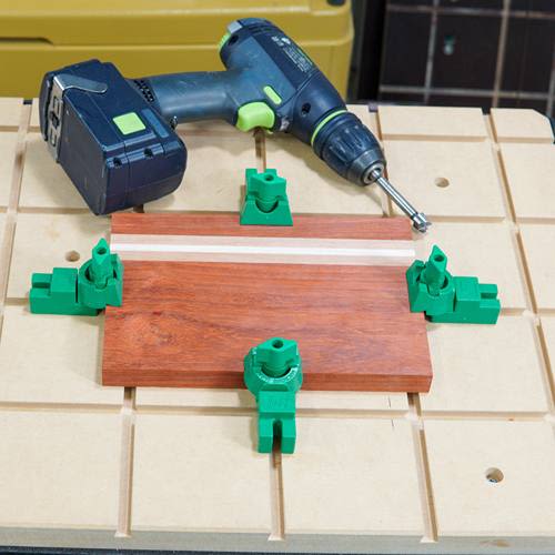 Green plastic clamp pads securing wood on a workbench next to a cordless drill for home improvement tasks