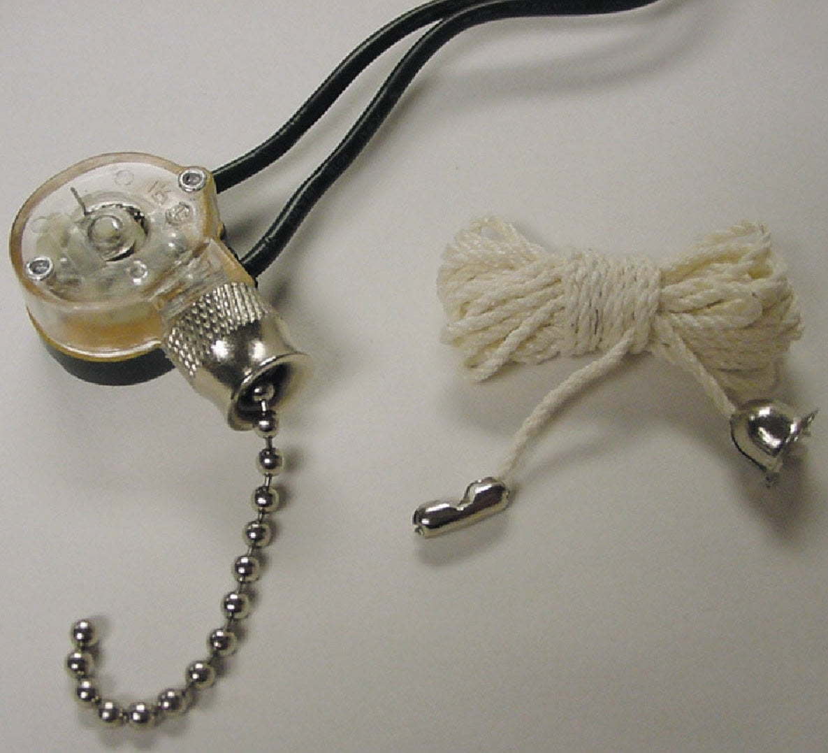 Single throw chrome pull chain switch with attached black wires and separate white braided pull cord for home improvement use