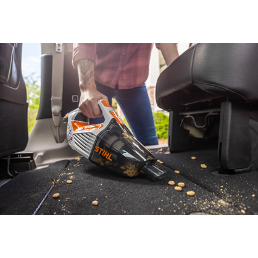 Person using handheld battery vacuum with orange and white design to clean debris from car interior carpet