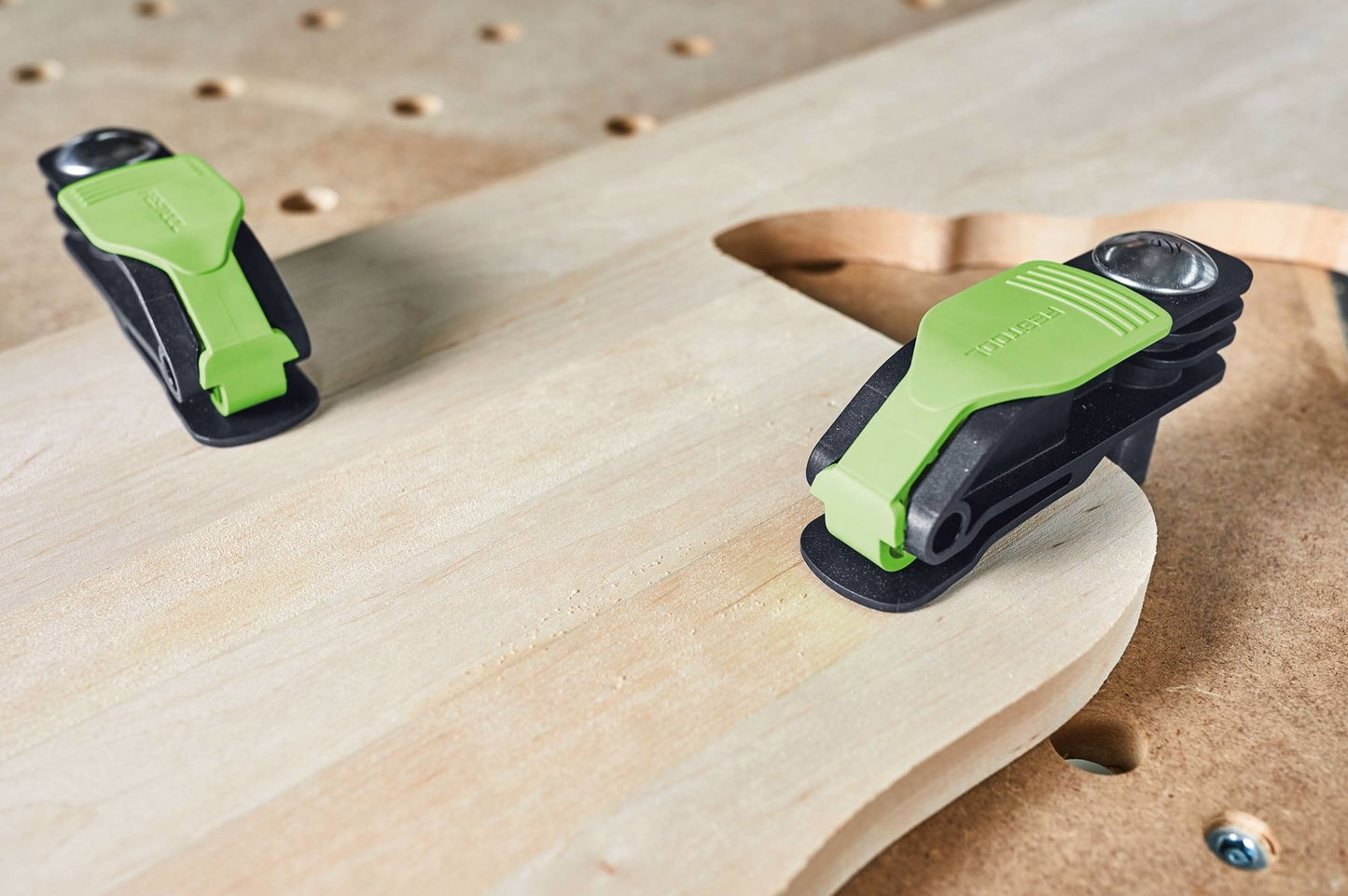 Green and black quick clamps attaching a wooden piece to a perforated workbench for woodworking projects