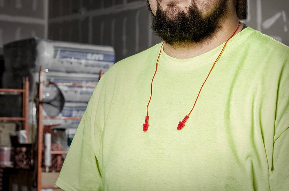Red corded reusable ear plugs worn around neck by man in neon yellow shirt on construction site for hearing safety