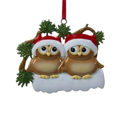 Two brown owls wearing red and white Santa hats sitting on snowy branch decorated with green pine leaves ornament