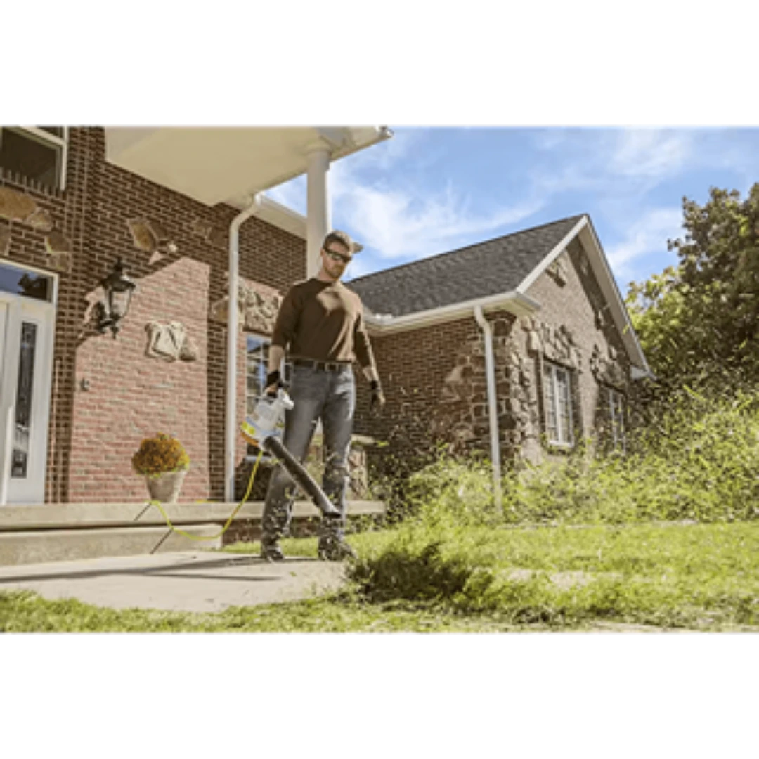 Man using STIHL electric handheld blower to clear grass clippings on a sidewalk in front of a brick house