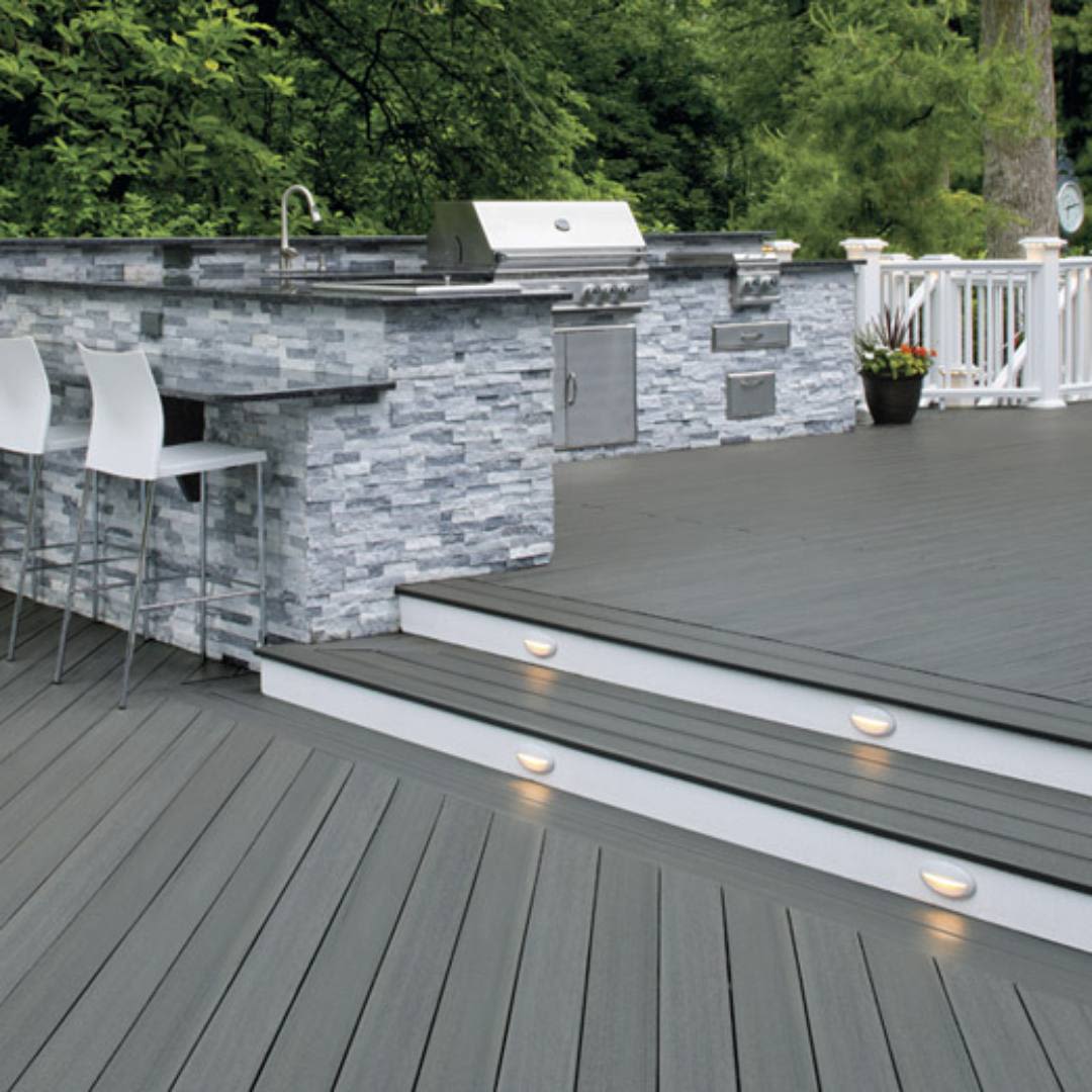 Outdoor kitchen area with gray composite decking and stone veneer bar featuring integrated lighting on steps